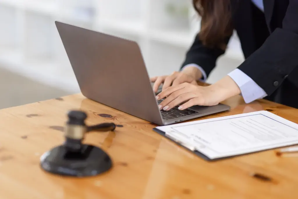 Person typing on a laptop next to a printed legal form and gavel while preparing a will