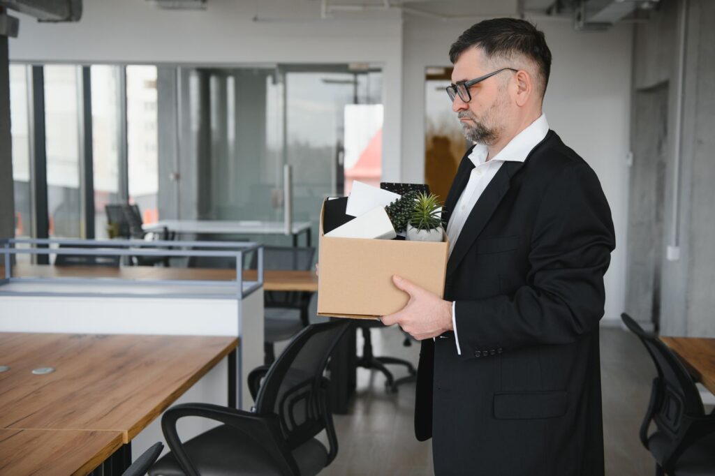 Man in a suit holding a cardboard box of belongings in an office