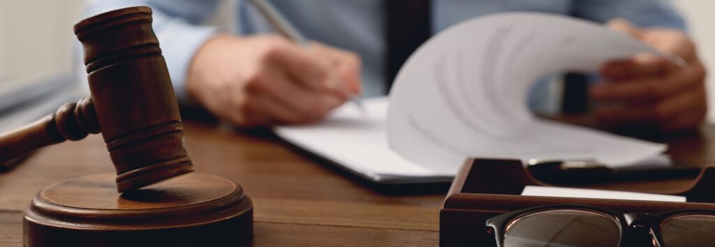 Wooden gavel on its sound block in front of a person reviewing papers at a desk