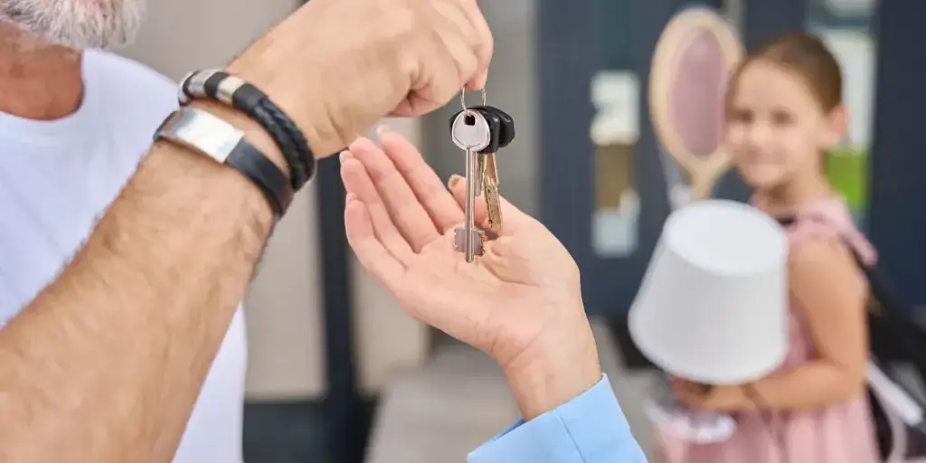 Parent handing house keys to an adult child outside a home while a grandchild waits nearby