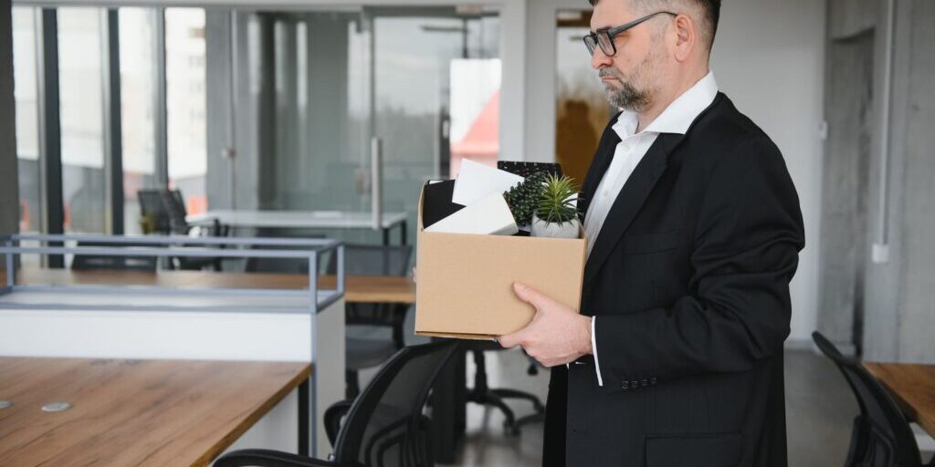 Man in a suit holding a cardboard box of belongings in an office