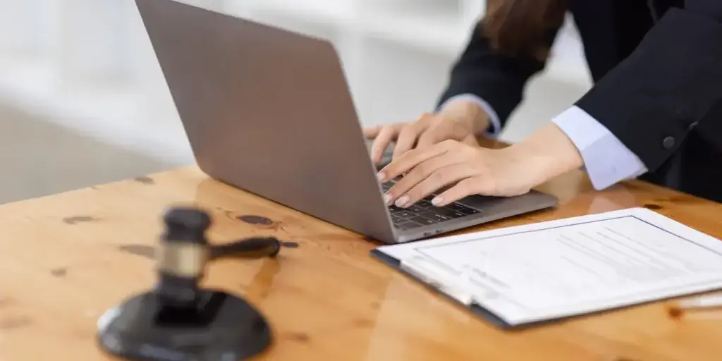 Person typing on a laptop next to a printed legal form and gavel while preparing a will