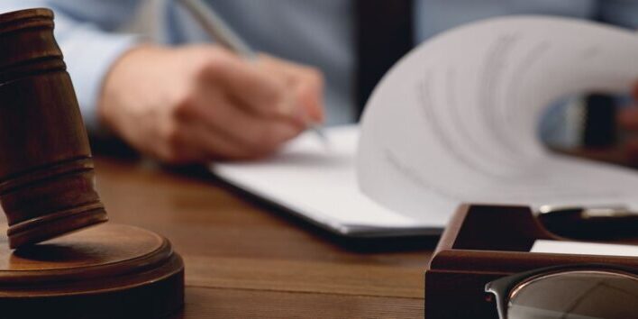 Wooden gavel on its sound block in front of a person reviewing papers at a desk